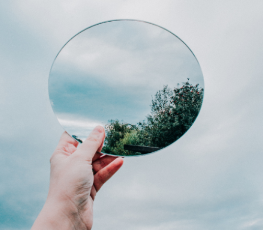 una mano muestra un espejo en el que se refleja parte del cielo en signo de transparencia y autenticidad.